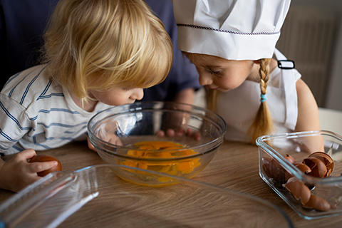 Zwei Kinder schauen neugierig in eine Schüssel mit Eiern