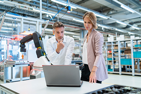 Geschäftsmann und -frau besprechen sich in einer modernen Fabrikhalle