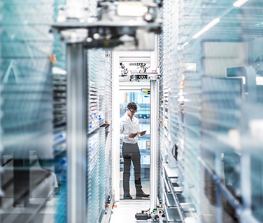 Mann mit Tablet steht in der Produktionshalle eines automatisierten Lagers