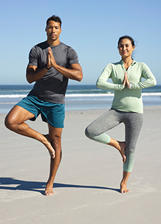 Jüngeres Paar macht Yoga am Strand