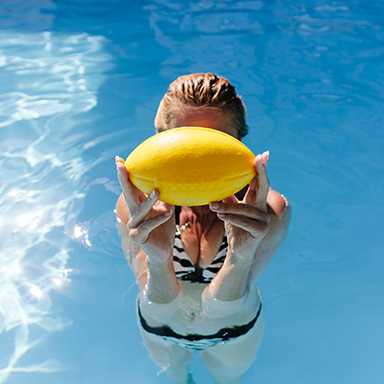 Frau im Bikini hält sich gelben Ball vors Gesicht