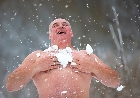 Erwachsener Mann reibt seinen nackten Oberkörper mit Schnee ein
