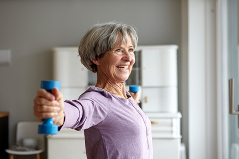 Ältere Frau trainiert lächelnd mit Hanteln