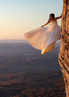 Braut mit weißem Kleid hängt an einer Steilwand