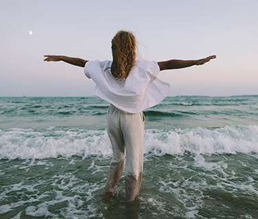 Frau läuft mit ausgebreiteten Armen ins Meer - Freiheit