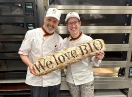 Ein Mann und eine Frau halten ein übergroßes Ciabatta mit der Aufschrift We love Bio in die Kamera