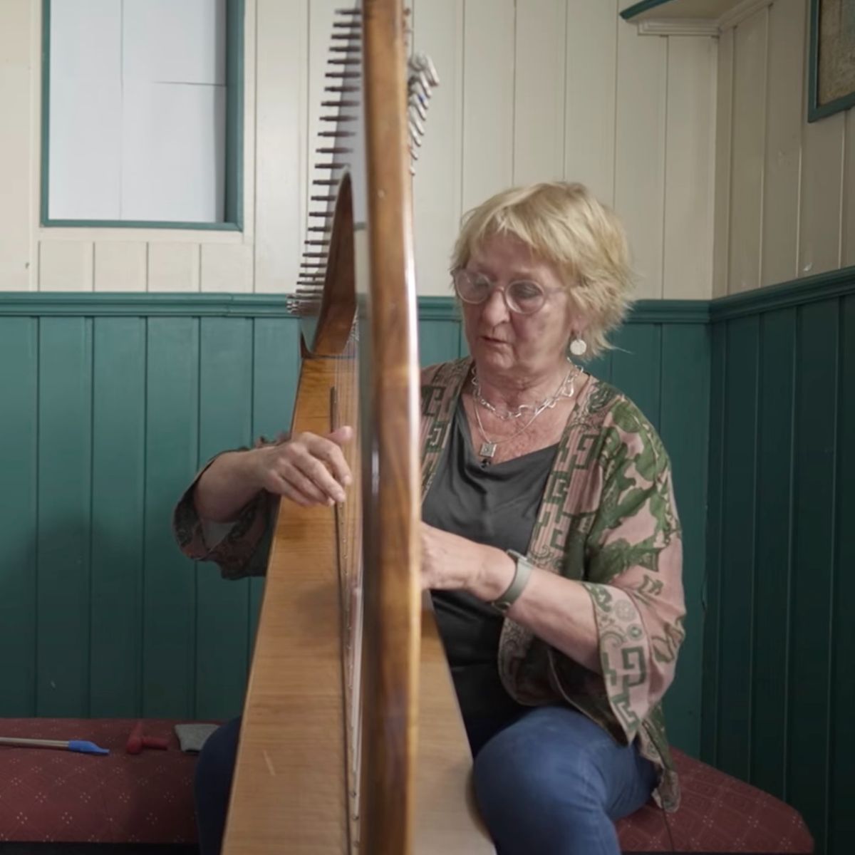 A woman with blonde hair and glasses playing a harp.