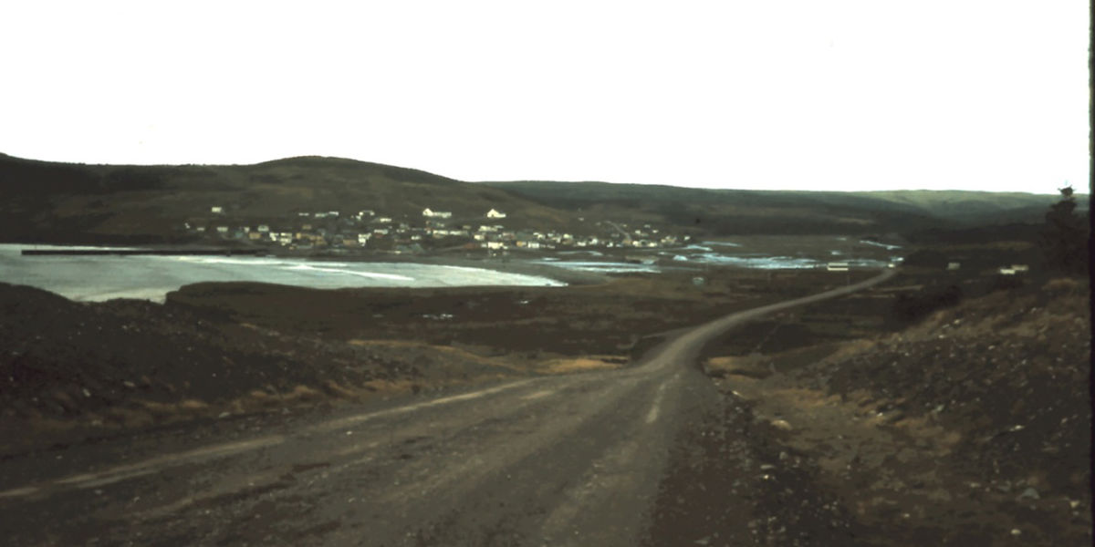 Landscape photograph of a harbour on a grey day, with some small green hills in the background.