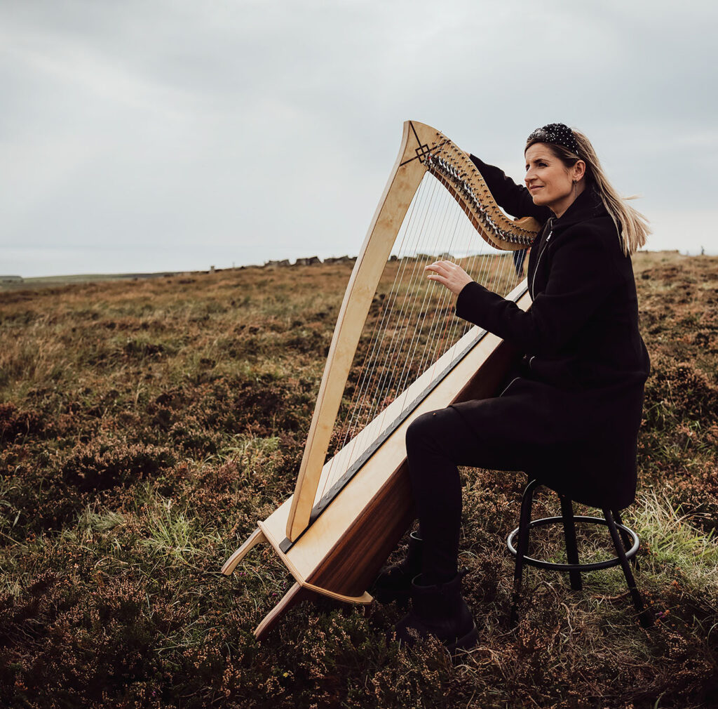 Elaine Hogan sitting outside in a rural setting with a harp, photograph by Philippe Gosseau