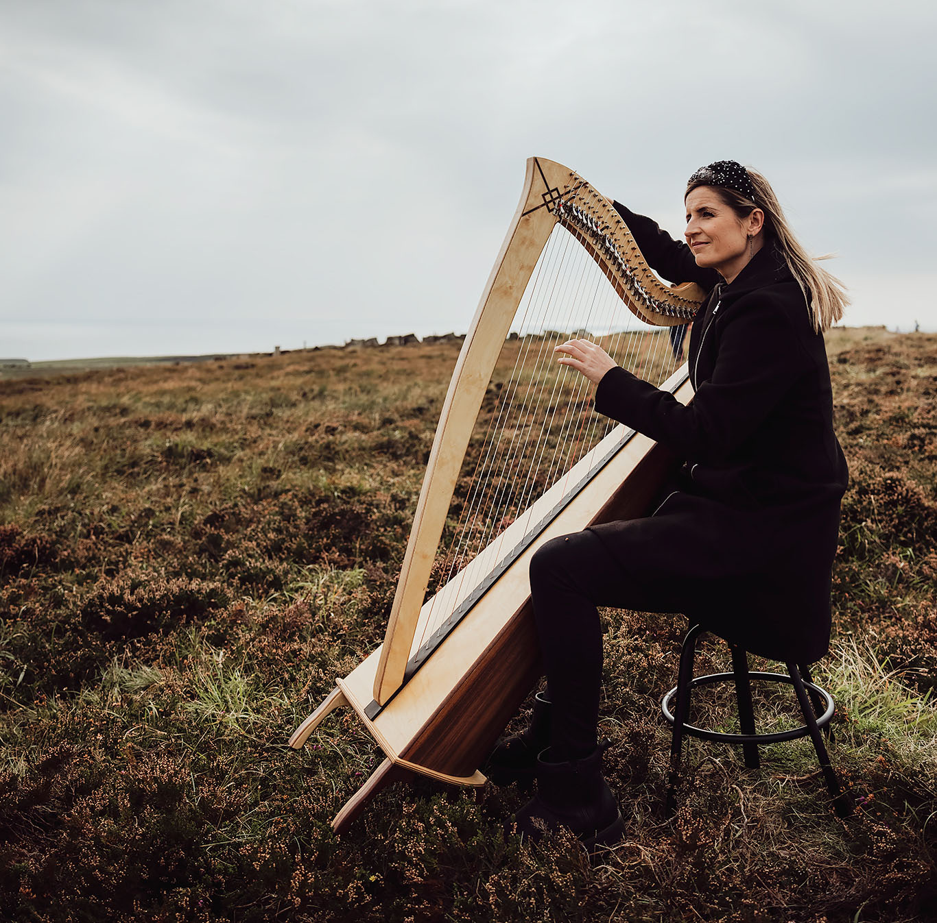 Elaine Hogan sitting outside in a rural setting with a harp, photograph by Philippe Gosseau