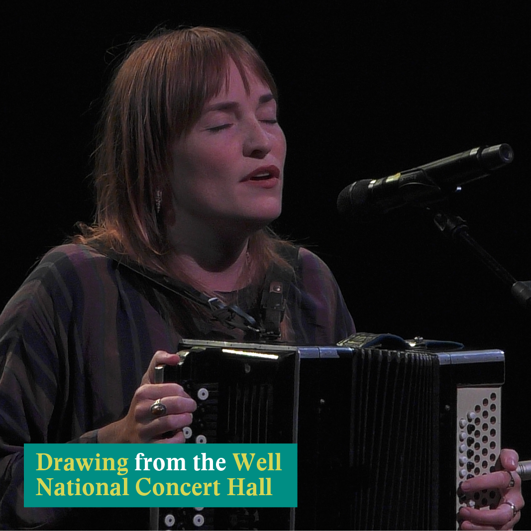A woman with red hair singing in front of a microphone with an accordion in her hands. In the bottom left corner of the image is a green box containing text that reads: "Drawing from the Well National Concert Hall"
