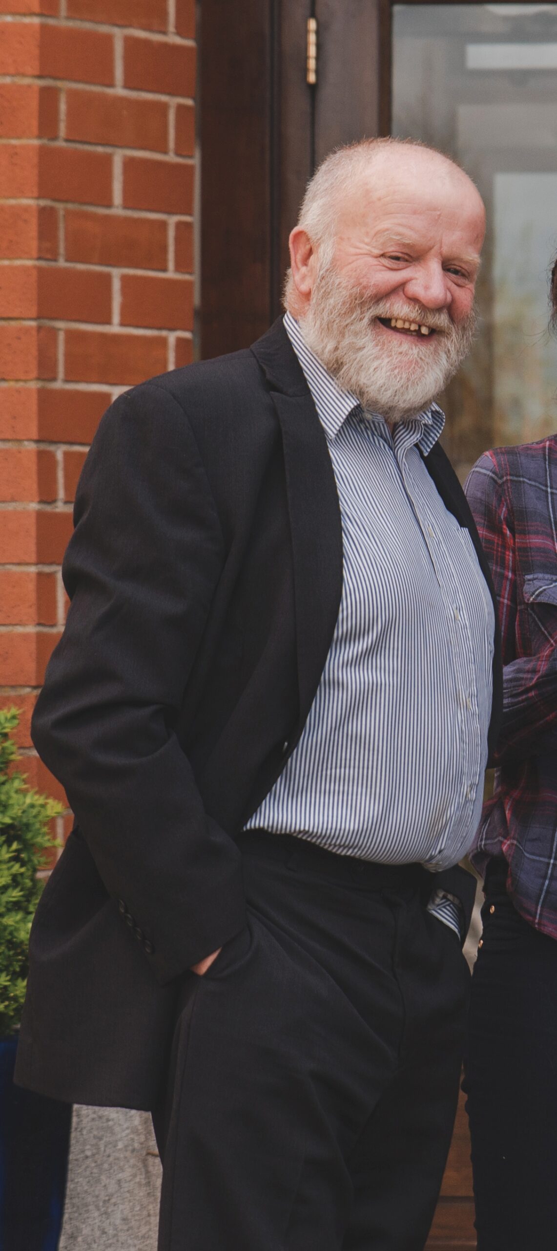 A man with white hair in a suit stands laughing