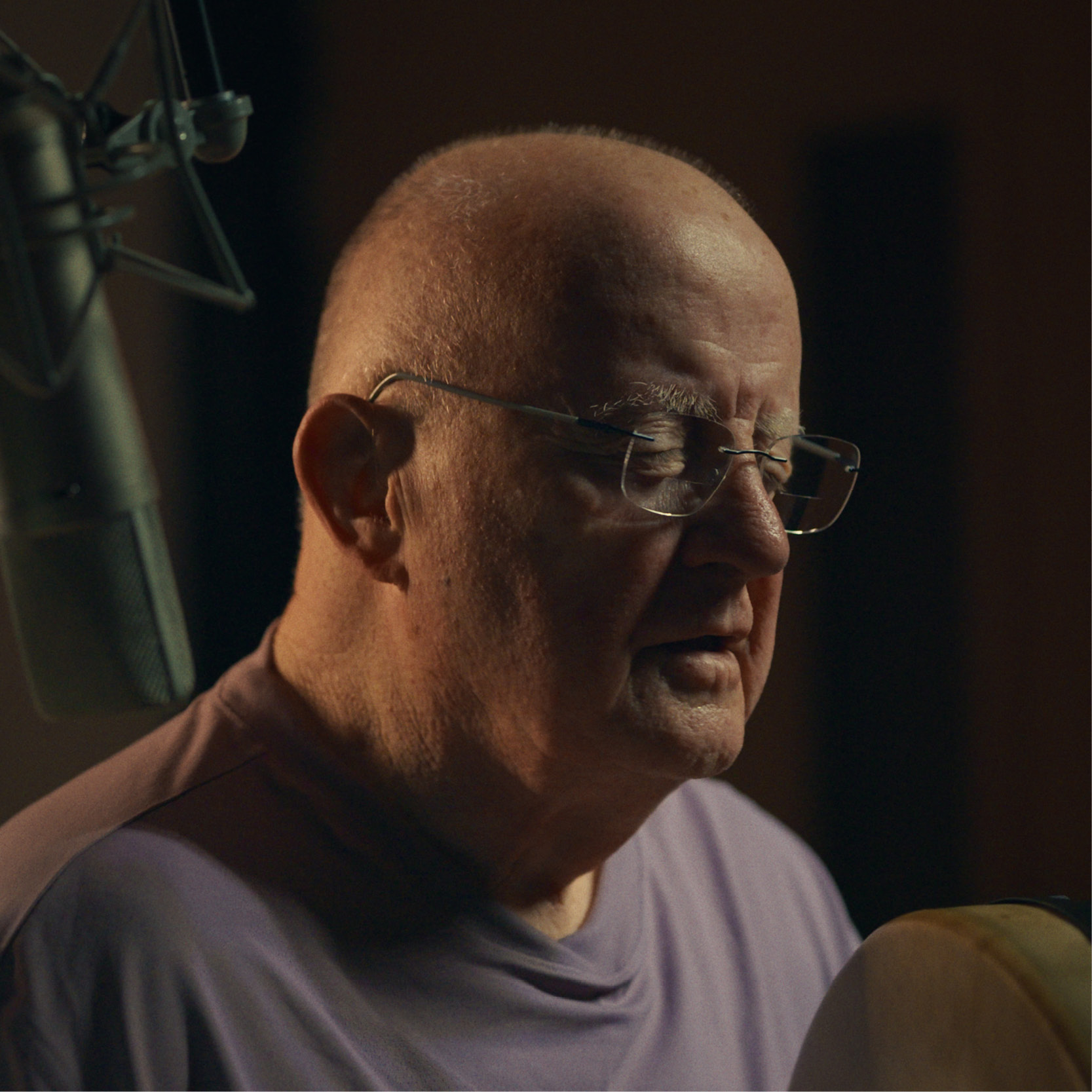 Christy Moore sits in front of a microphone, holding a bodhrán