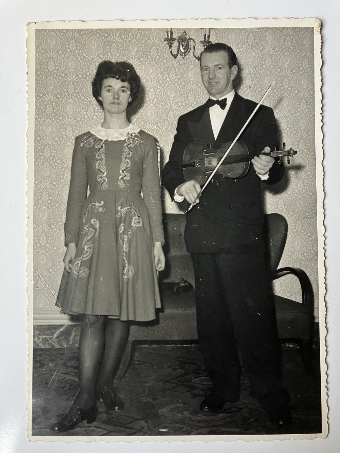Black and white photo of a woman in a dress standing next to a man in a suit holding a fiddle.