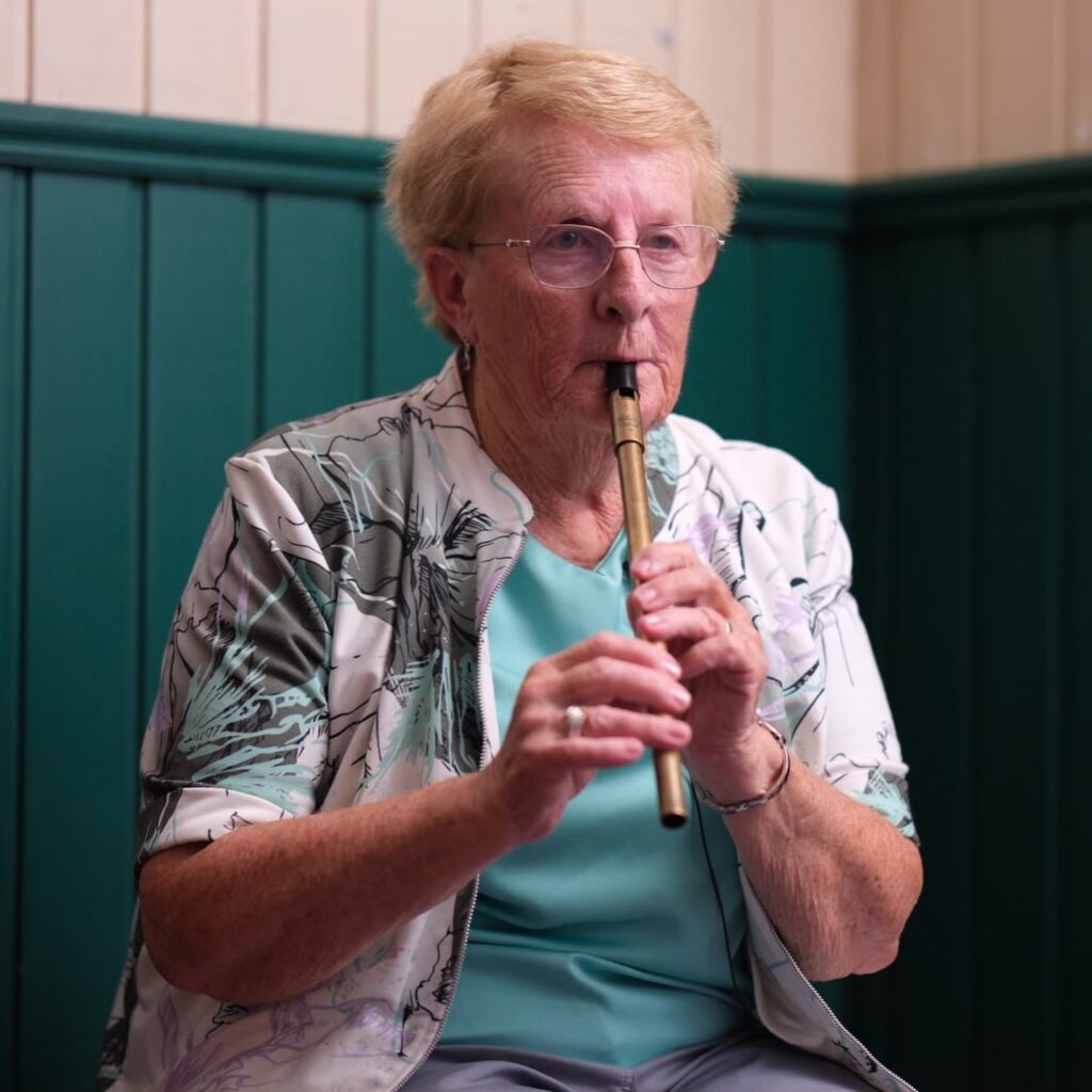 A woman wearing glasses sitting in a pub playing the tin whistle.