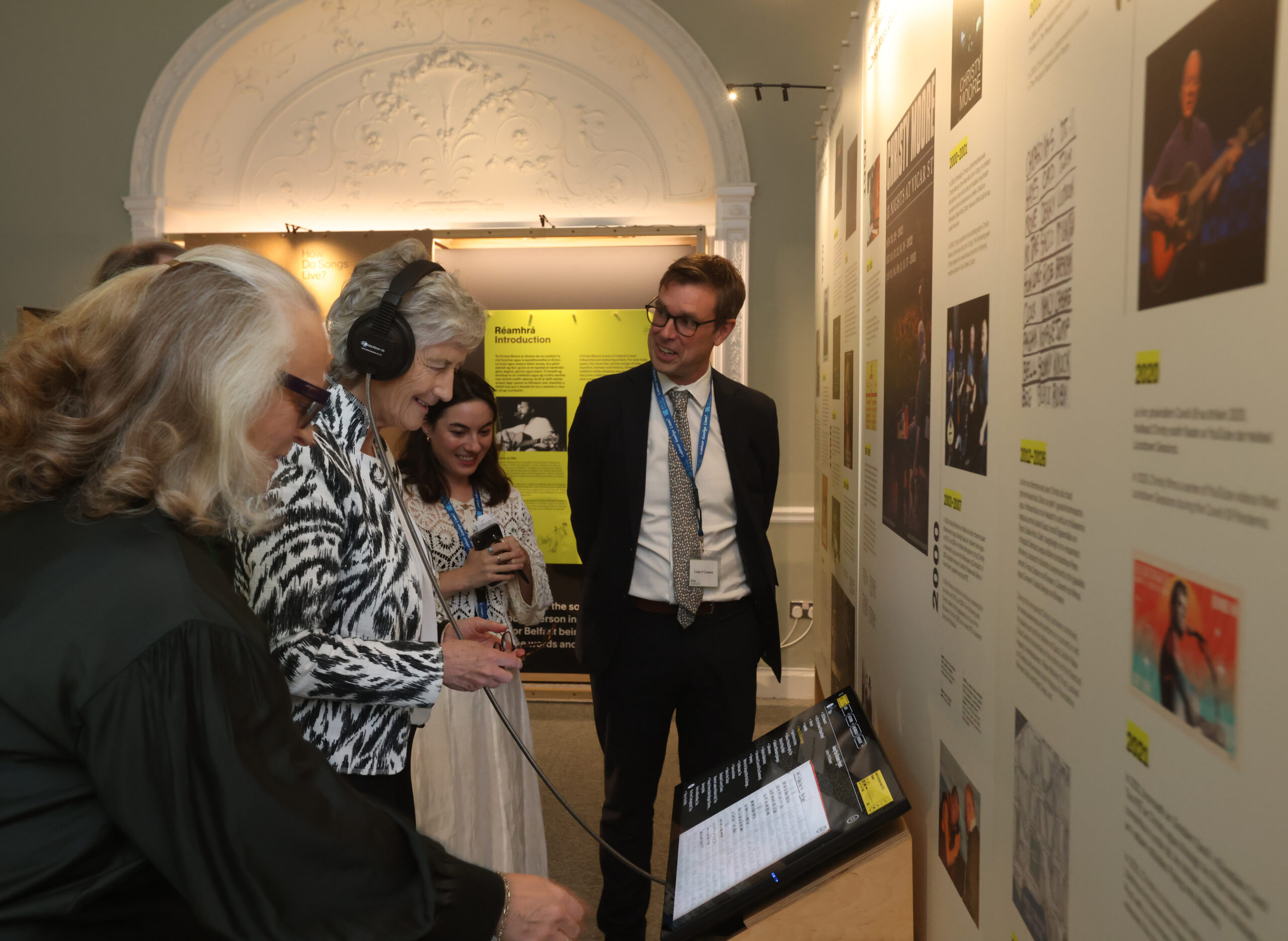 A woman wears headphones and loooks at an interactive touch screen positioned beside museum posters.