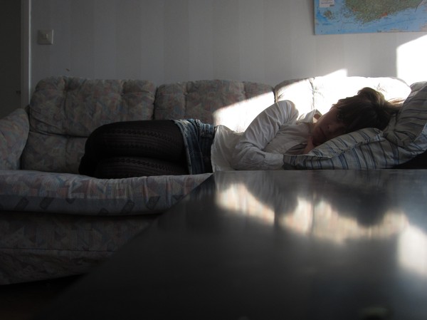 Kvinna som ligger på soffa, ljusspeglingar i bordet framför henne.