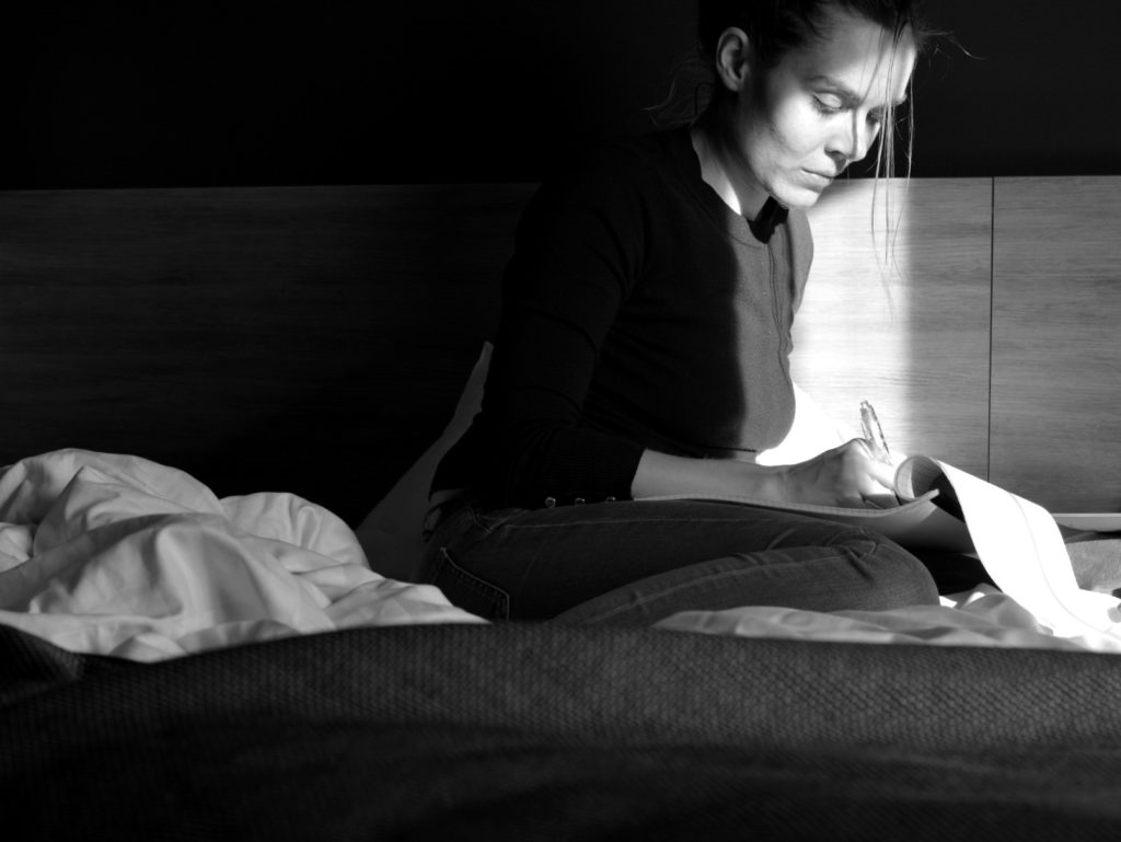 Ulrika Nettelblad skriver i skrivblock på hotellsäng, svartvit bild.