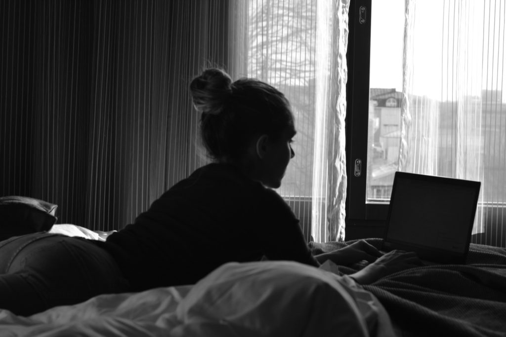 Ulrika Nettelblad som skriver på laptop på hotellsäng, svartvit bild.