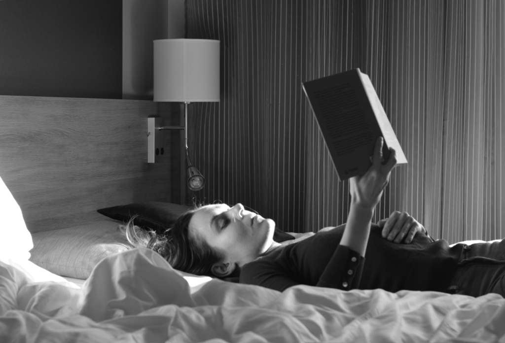 Ulrika Nettelblad läser bok på hotellsäng på Hotell Pommern. Svartvit bild.