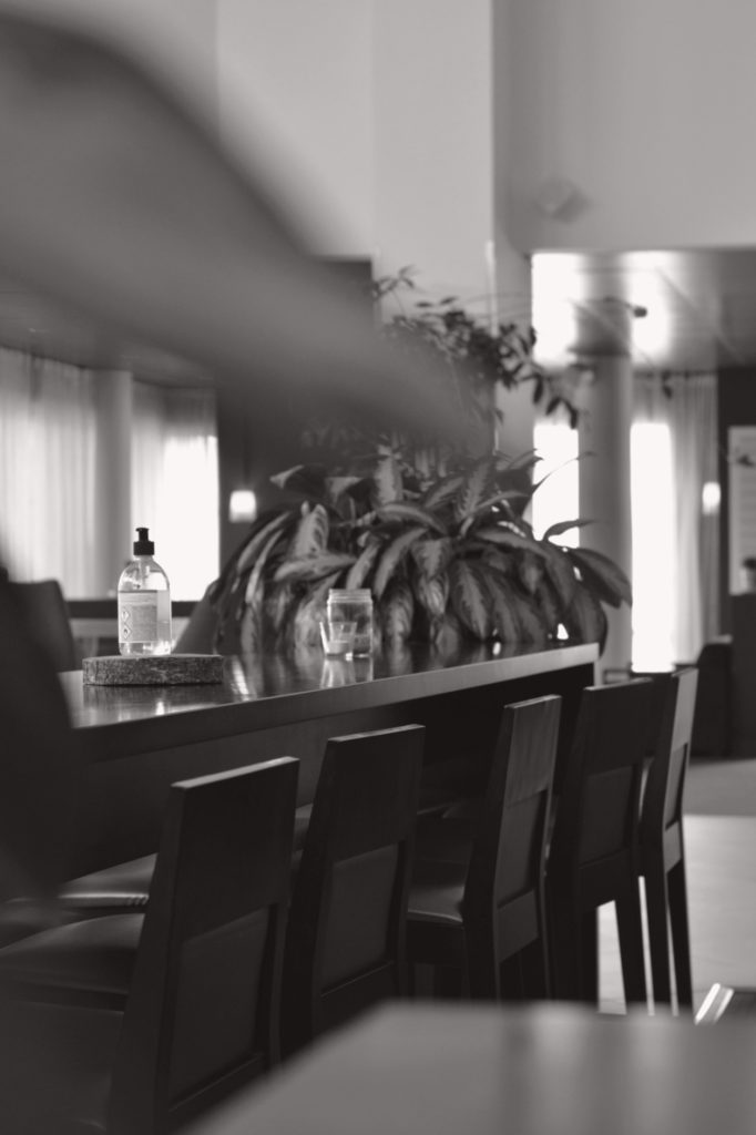 Svartvit bild med sepiatoner på bord, stolar och handsprit i lobbyn på Hotell Pommern.