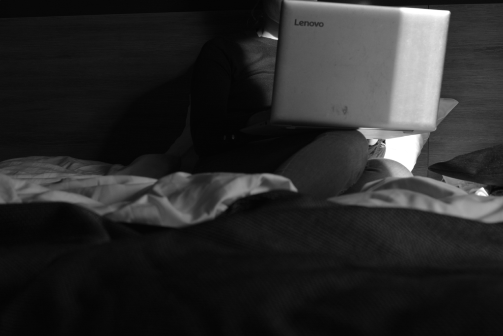 Laptop i knä på hotellsäng, svartvit bild.
