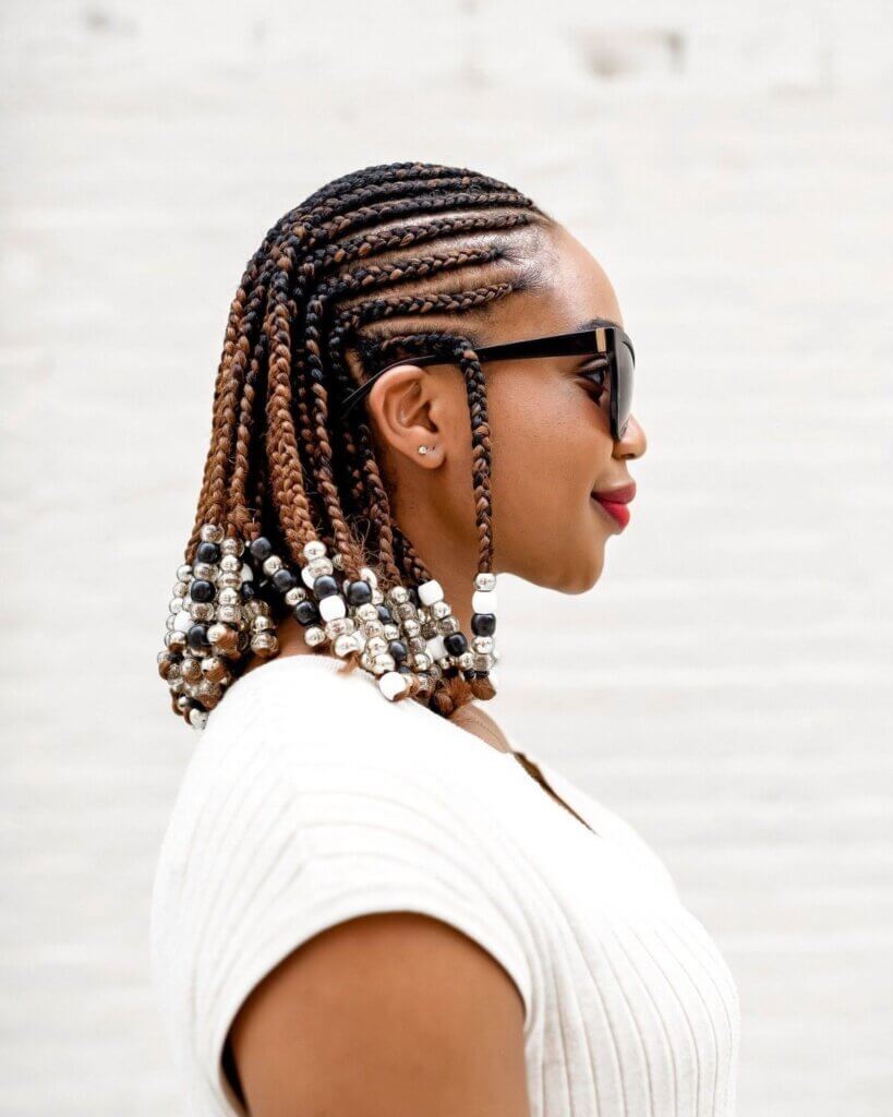 This image features a woman with a stylish "2 Step" attachment hairstyle. The hair is intricately braided close to the scalp, leading to medium-length braids adorned with a variety of beads in silver, black, and white. The overall look is both fashionable and refined, making it an excellent choice for those seeking unique and elegant attachment hairstyles