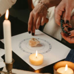 Two women looking at a birth chart, surrounded by candles and crystals by Polina Kuzovkova via Unsplash+