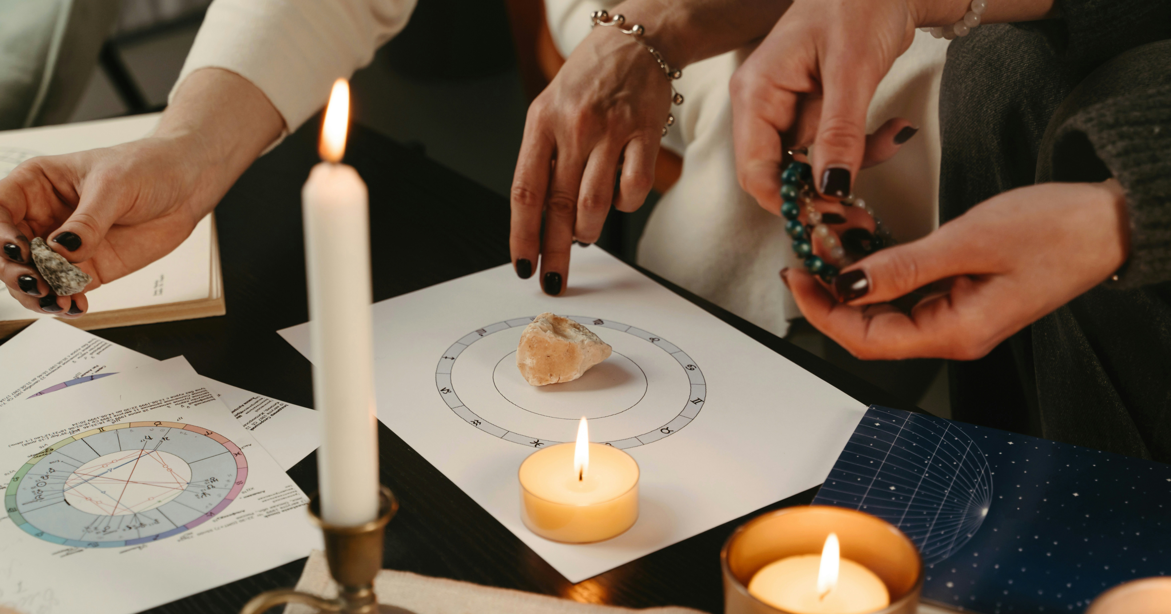 Two women looking at a birth chart, surrounded by candles and crystals by Polina Kuzovkova via Unsplash+