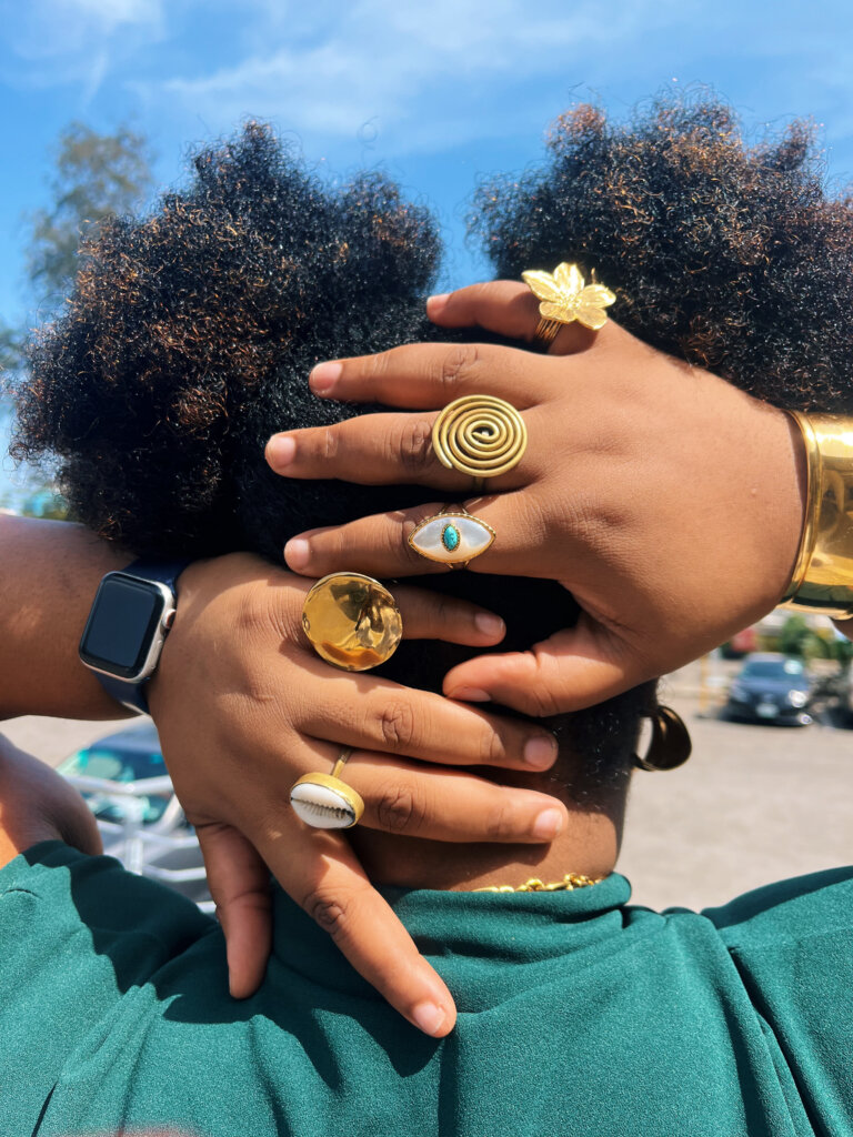 Ag. Managing Editor Denise Eseimokumoh’s jewellery for The Guardian Woman Festival. She is wearing a cowrie ring, a gold circle ring, an eye of horus ring, a spiral ring, and a flower ring, with a gold wrist cuff and Apple Watch held behind her hair, which is in pigtails by Denise Eseimokumoh