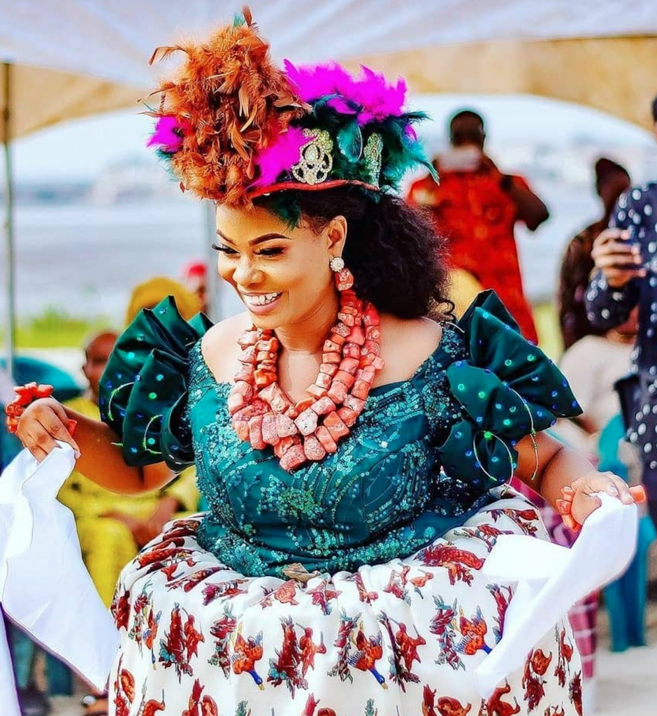 A beautiful, full-figured Ijaw bride wearing a green blouse and double wrapper, colourful headgear, and stacks of coral beads via @ijawweddings on Instagram