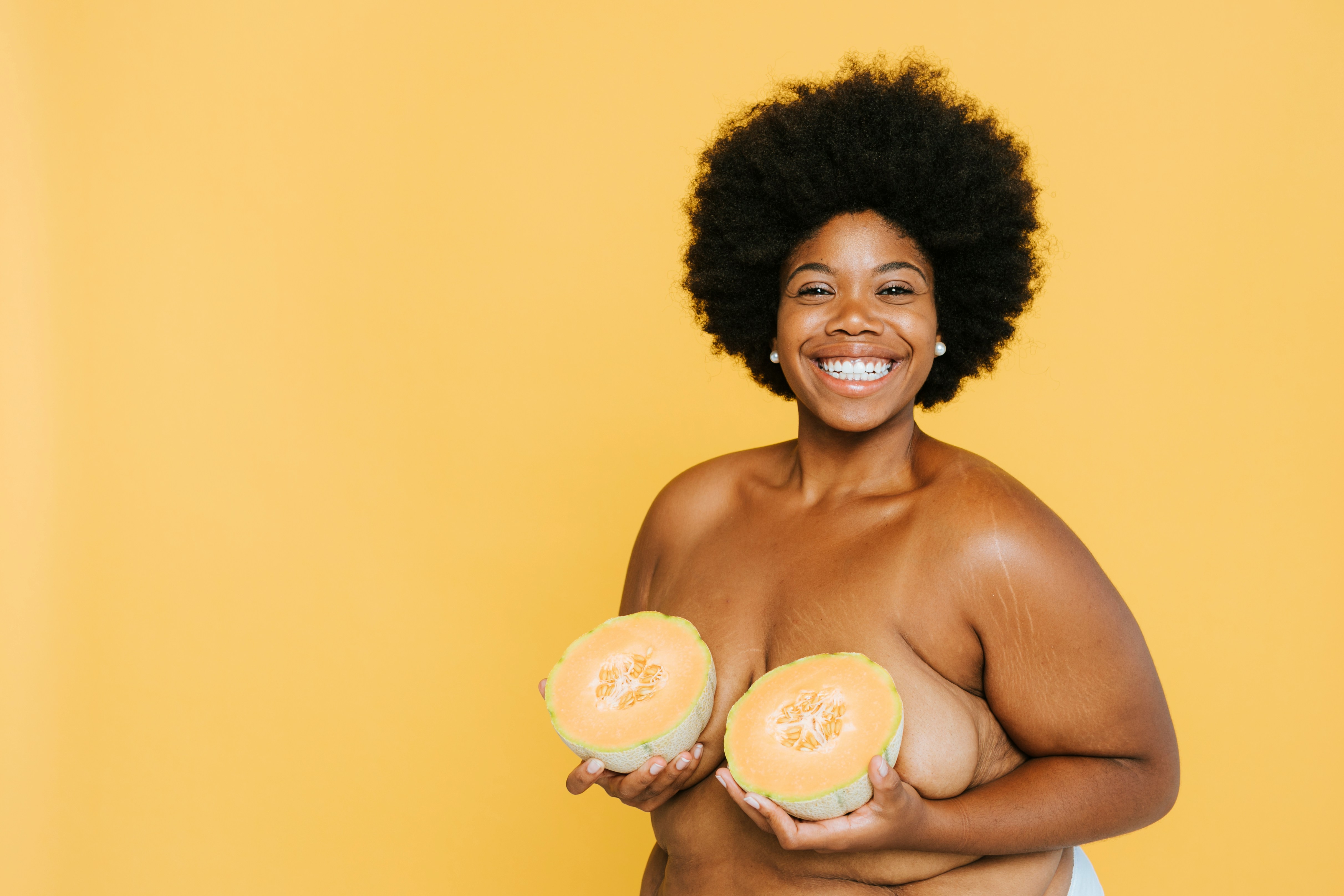 A braless black woman holding two cantaloupes covering her breasts by Curated Lifestyle via Unsplash+