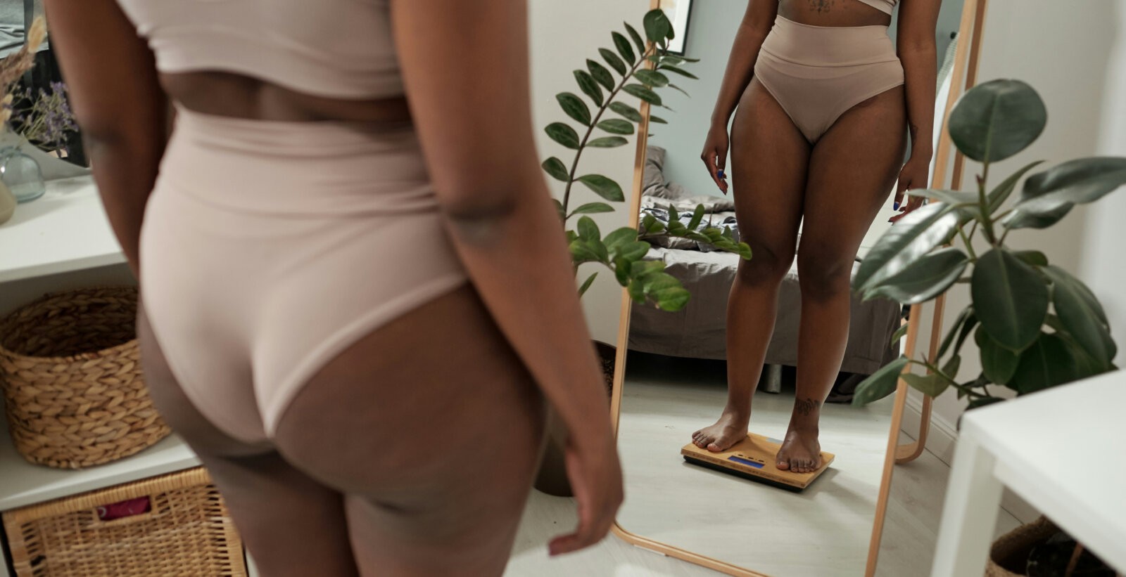 Body image; a black woman standing on a scale in front of the mirror via Getty Images on Unsplash+