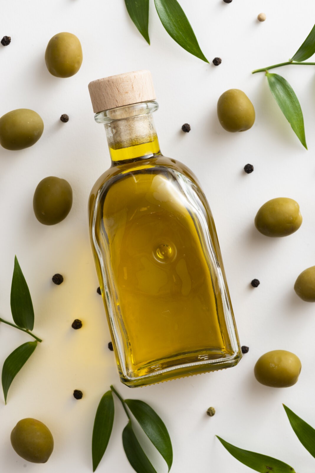A small bottle of olive oil surrounded by olives via Freepik