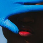 A black woman wearing a blue glove and covering her face via Unsplash