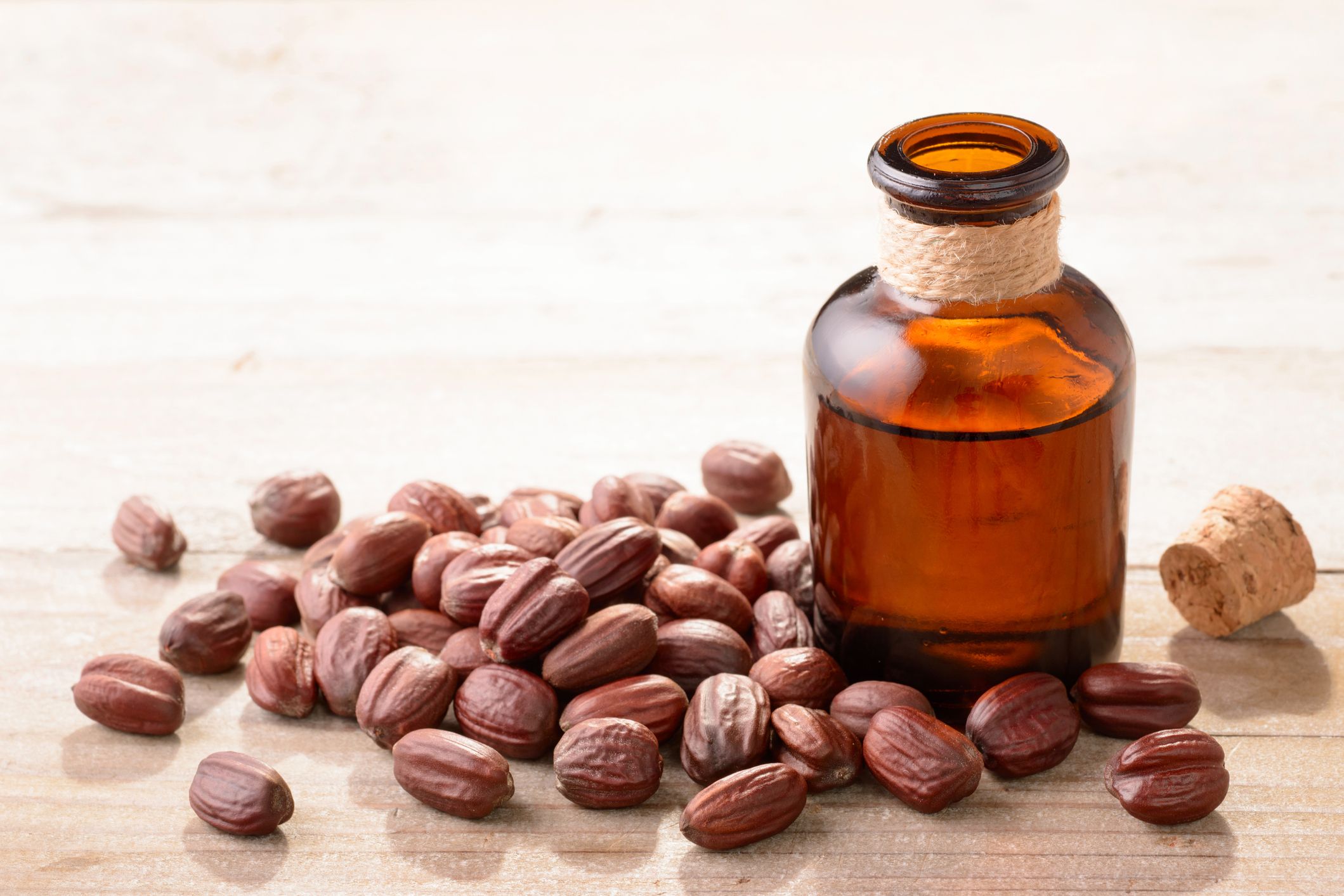 A small brown bottle of jojoba oil pictured with jojoba seeds via prevention.com
