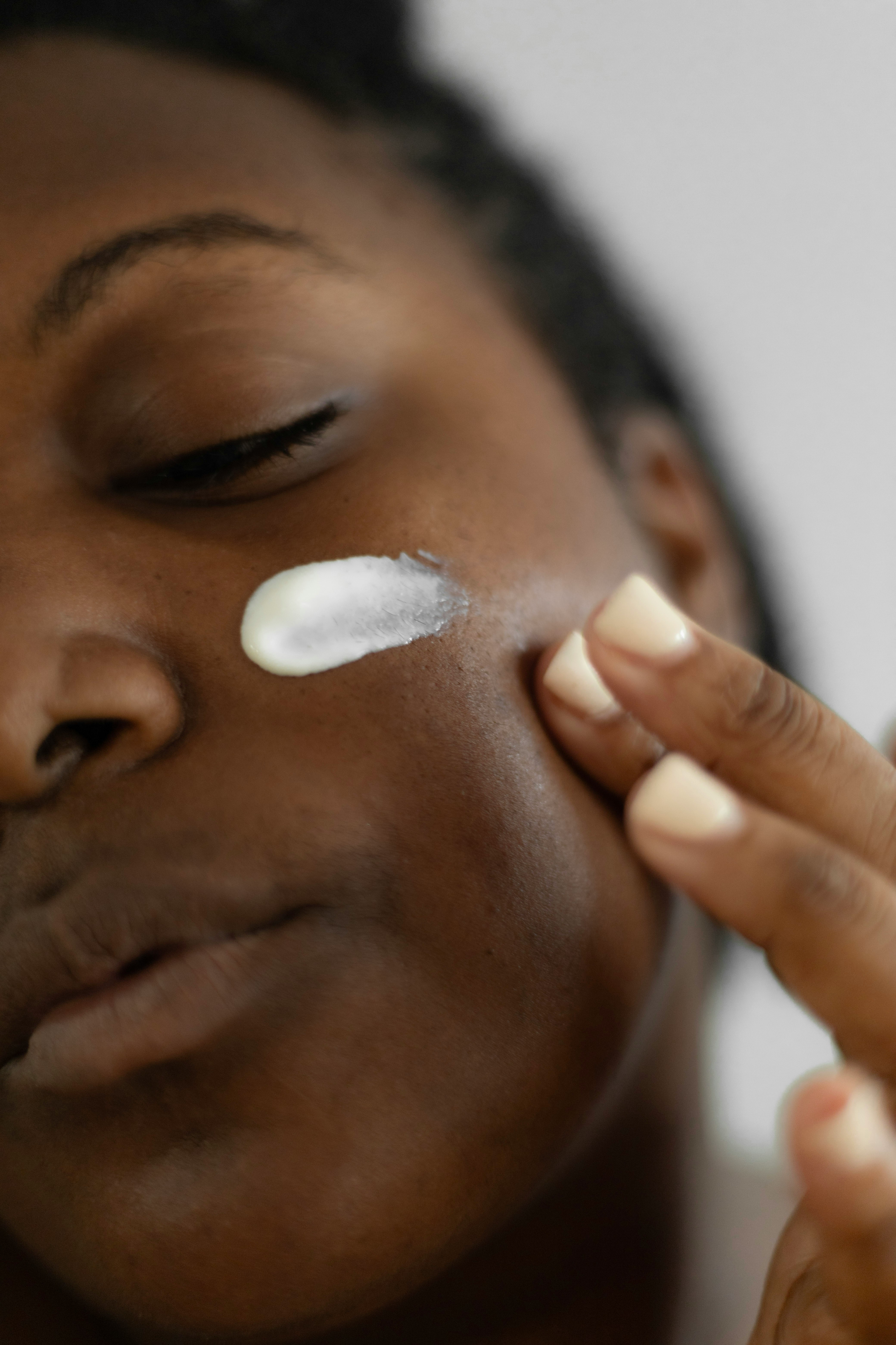 A close up shot of black woman applying sunscreen to her face via Leighann Blackwood via Unsplash