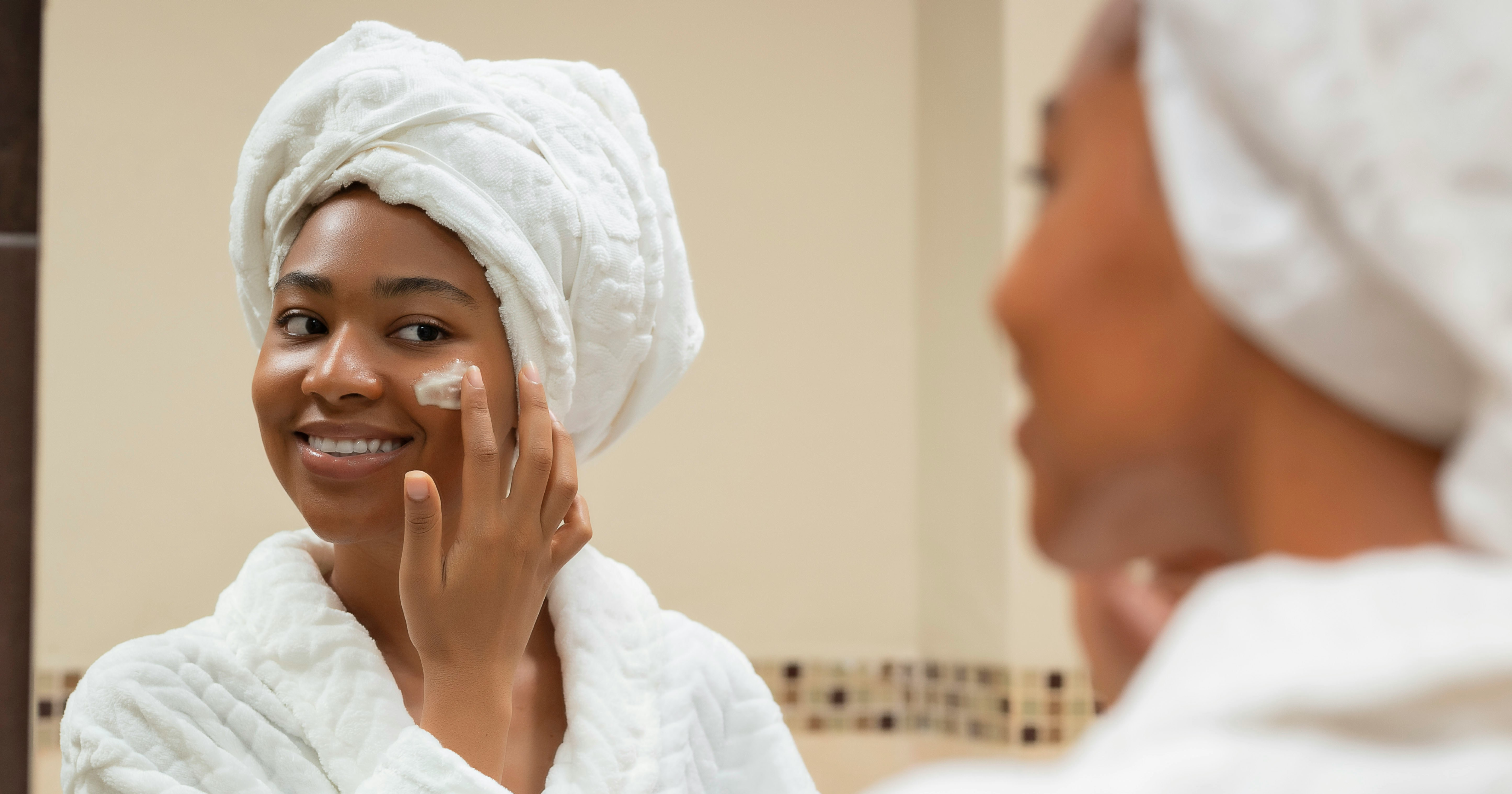 A black woman in a robe applying sunscreen to her face by Kaeme via Unsplash