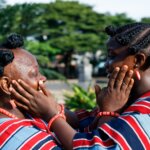 Two women with native hairstyles touching each other’s faces tenderly