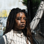An angry-looking black woman standing in the shadow of a chain-link fence via Freepik