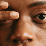 Close up shot of a black woman with two fingers over her left eye by AC via Unsplash