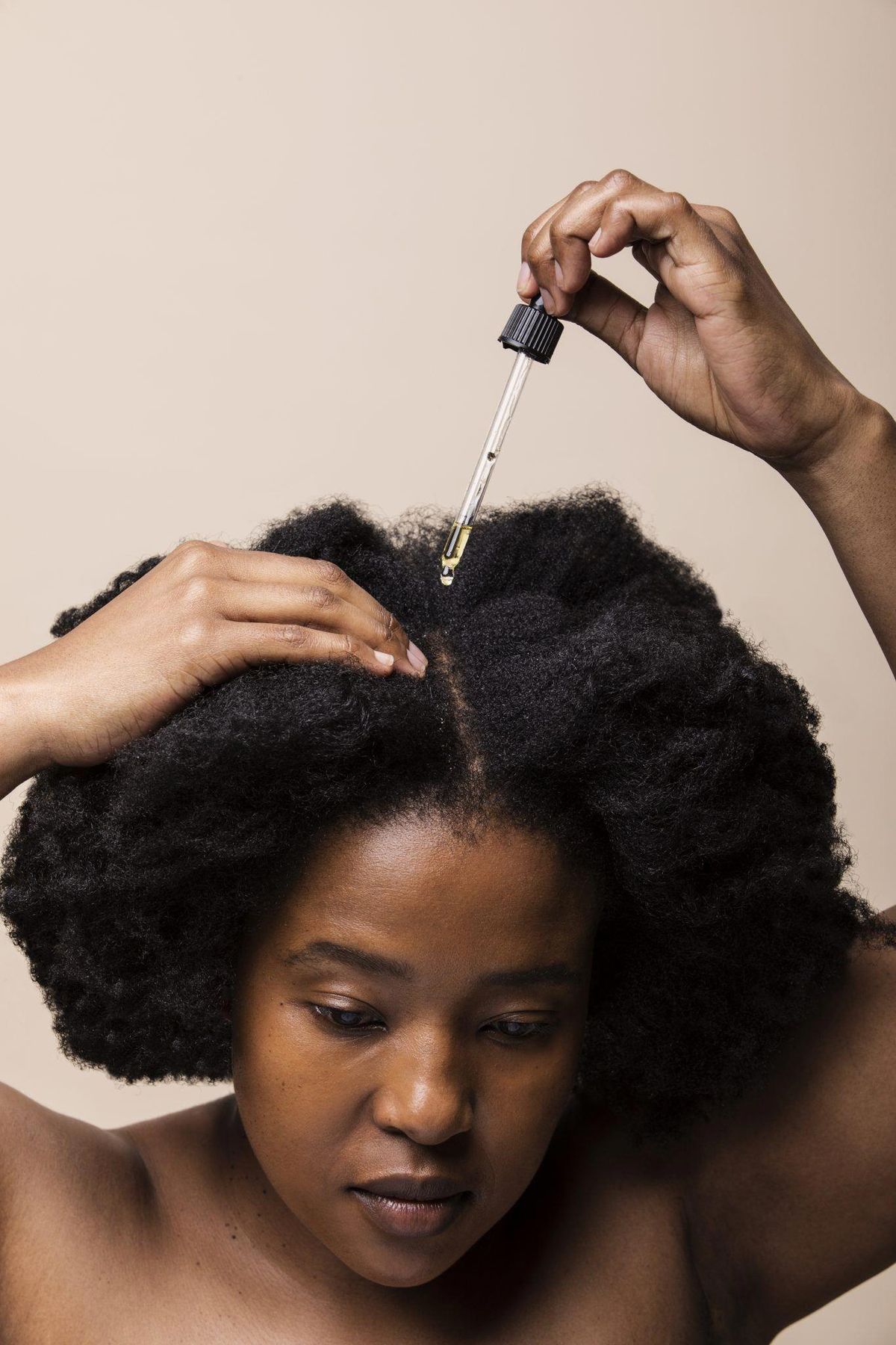 A black woman applying serum in her hair via Pinterest.