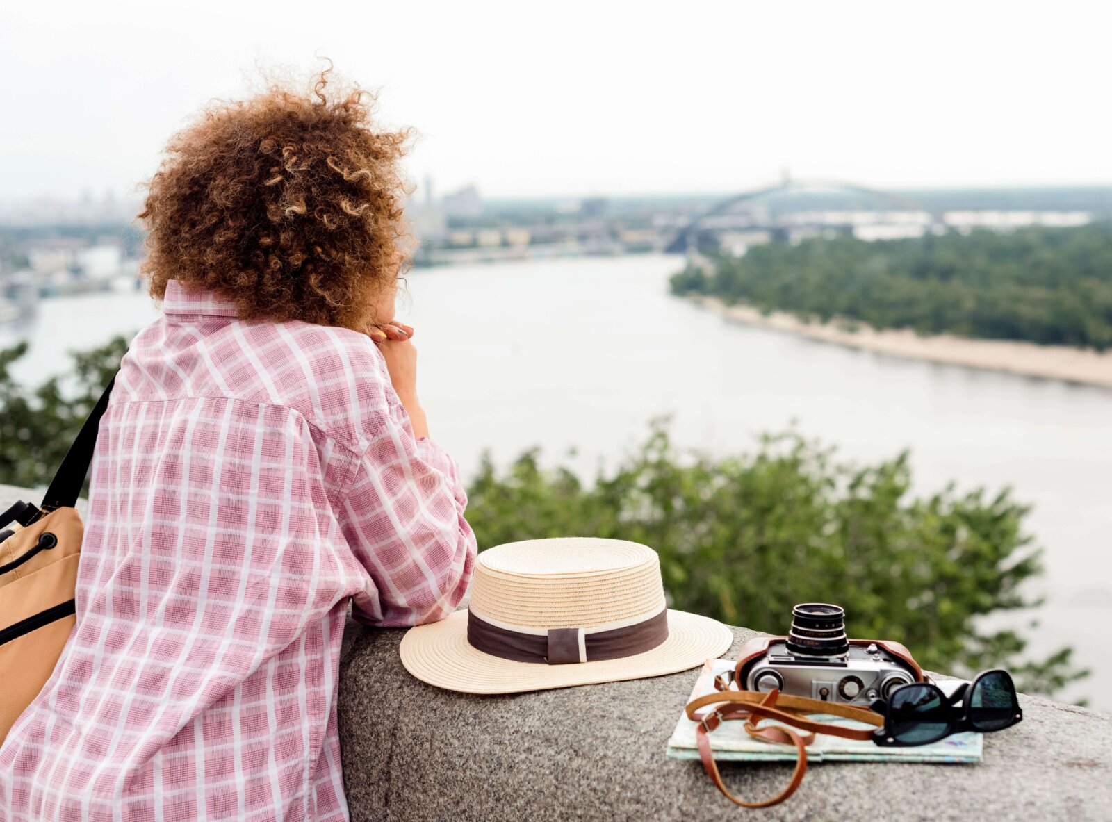 Woman leaning on a bridge with a hat, sunglasses and camera via Freepik