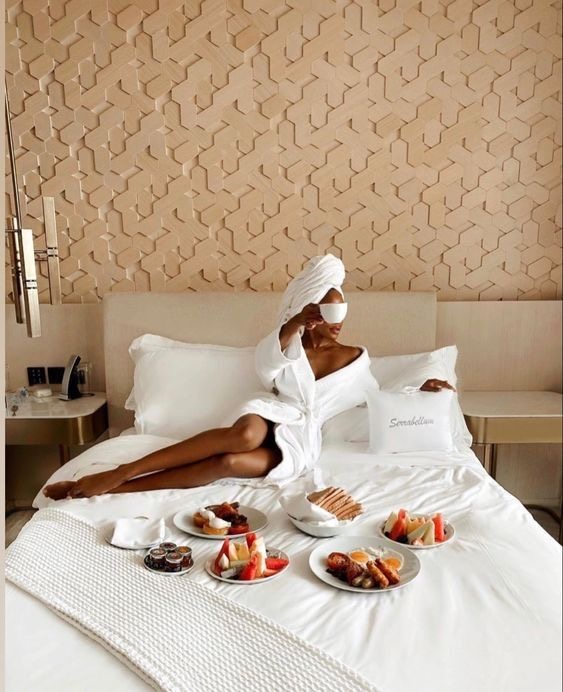 Black woman in a white robe lying on a bed with a full breakfast spread by Brittany Bournes via Pinterest