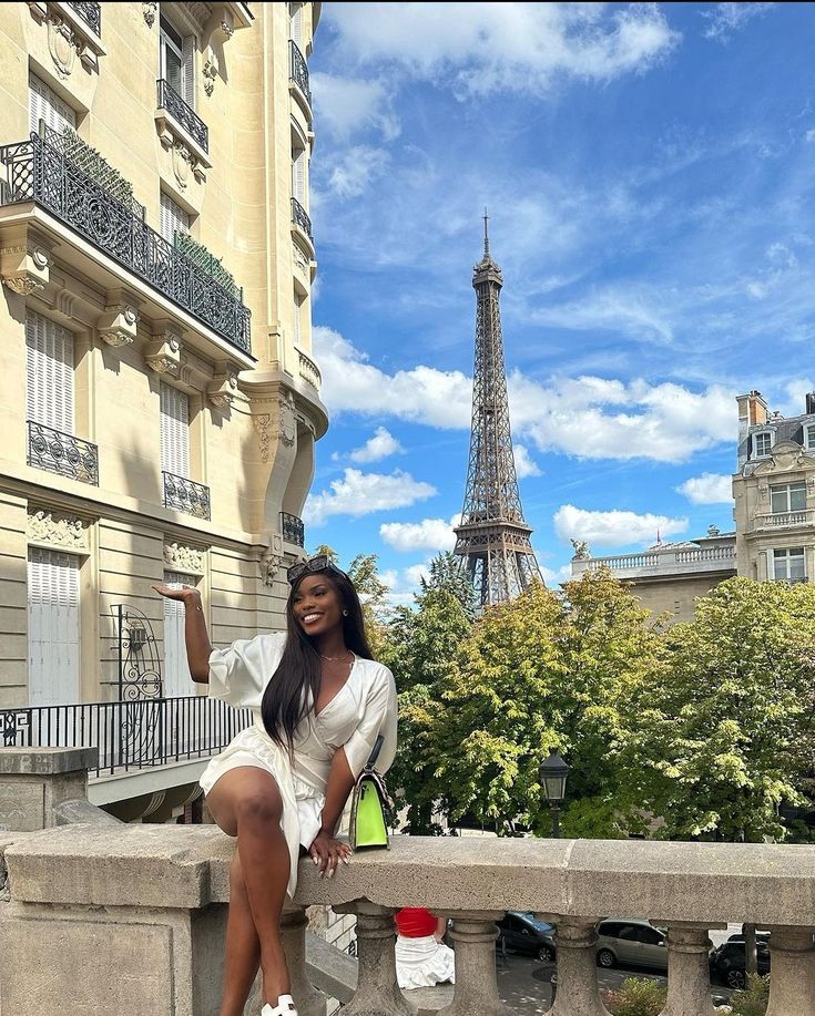 A black woman sitting on a street block in Paris, with the Eiffel Tower in the background via Pinterest. 