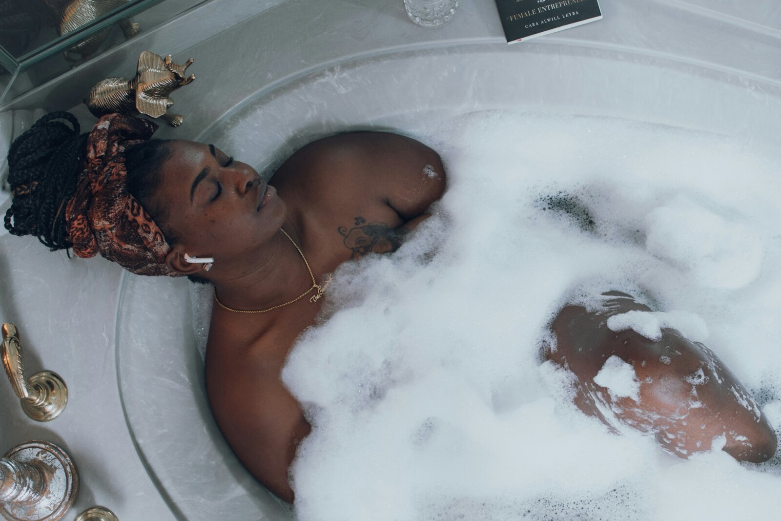 Black woman relaxed in a bathtub with earplugs plugged in by Brandy Kennedy via Unsplash