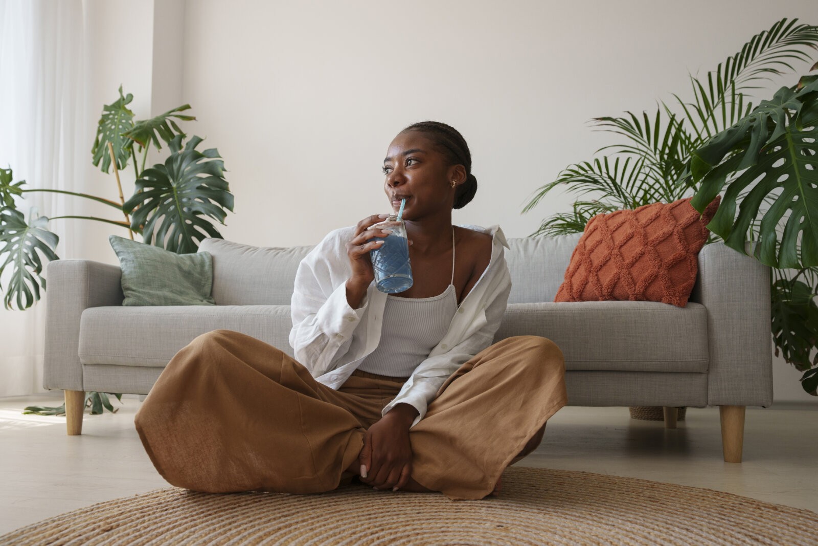 Black woman sipping a drink while sitting on the floor in her home via Freepik