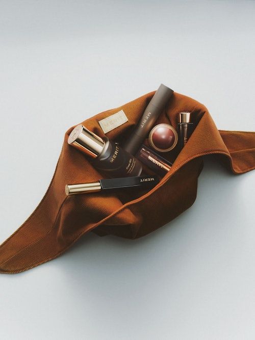 A brown makeup bag filled with Merit makeup products via Scarymommy.com