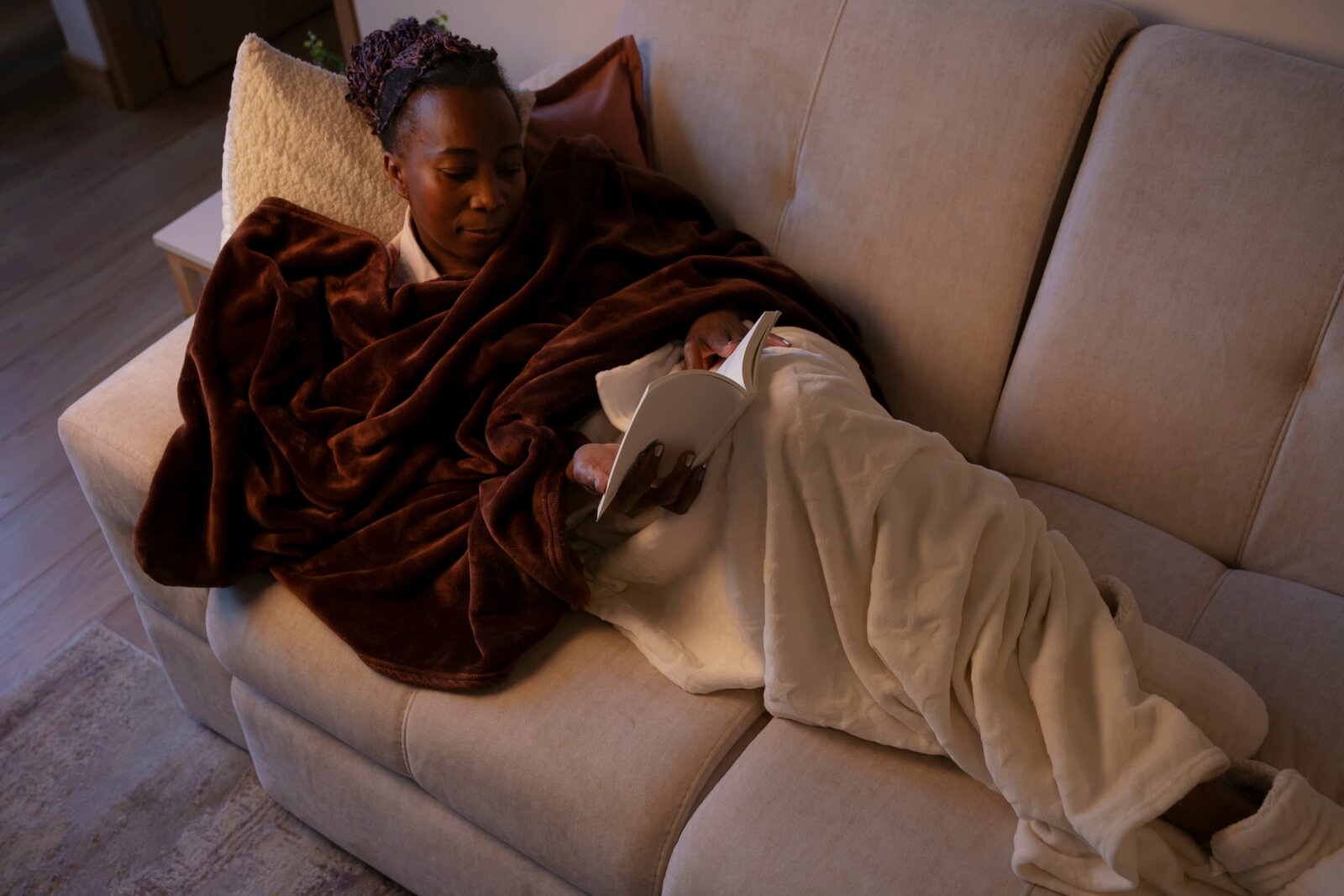 Black women lying on a couch covered with a blanket and reading a book by Pablo Merchan Montes via Unsplash