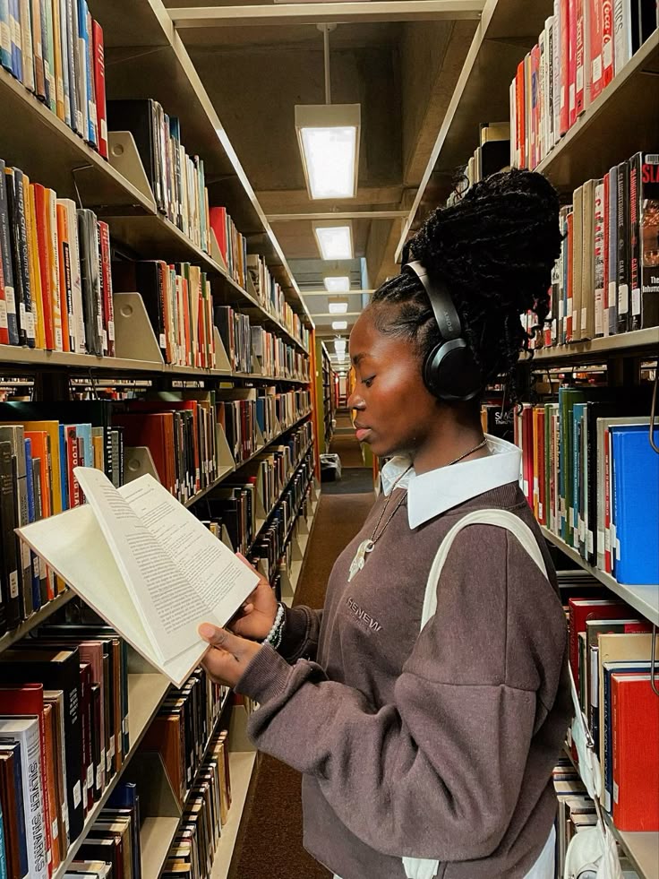 A Black woman reading in between shelves of books in a library via Pinterest. 